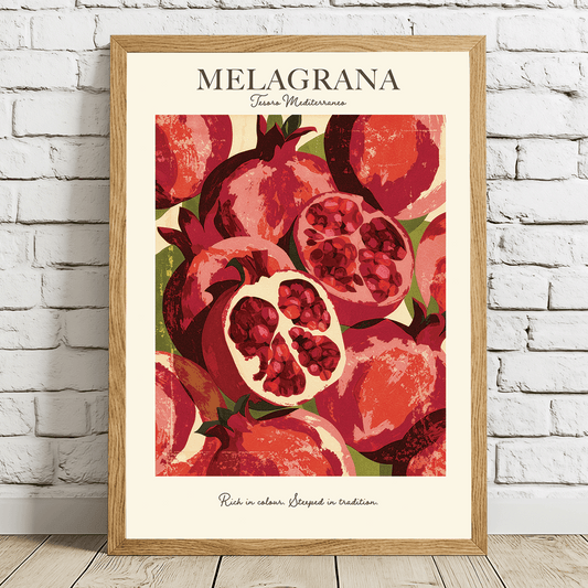A framed art print featuring a stylized illustration of red pomegranates with the text 'MELAGRANA' at the top, leaning against a white brick wall on a light wood floor.