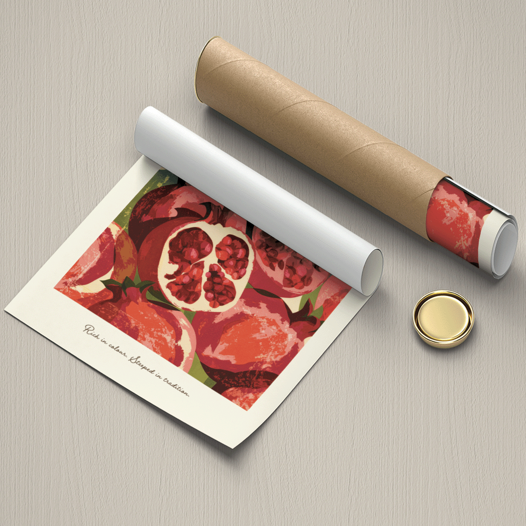 A rolled art print or poster showing a watercolor-style pomegranate illustration, displayed alongside a brown cardboard mailing tube and a small round gold cap on a light gray textured surface.