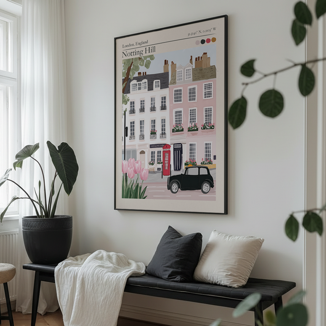 Framed artwork of a street scene with houses and a car on a wall in a room with a bench and plants.