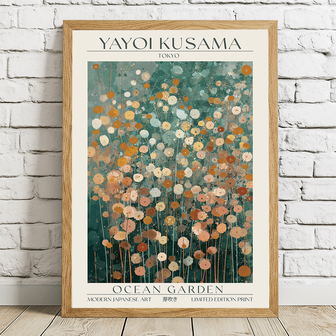 A framed art print of Yayoi Kusama's 'Ocean Garden' poster, leaning against a white brick wall on a light wooden floor. The print features a cream background with a central teal and orange floral pattern, enclosed in a light wood frame.