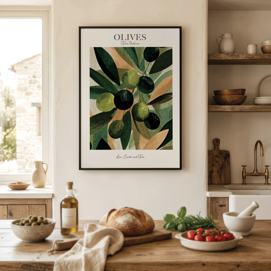 A framed art print featuring a botanical illustration of green olives on a branch, with the text 'OLIVES' at the top and 'Love, Care and Time' at the bottom, displayed on a warm beige wall in a rustic kitchen setting with food props on a wooden table.