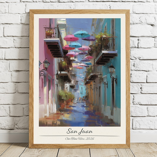 Framed artwork of a colorful street scene with umbrellas in San Juan, displayed on a white brick wall.