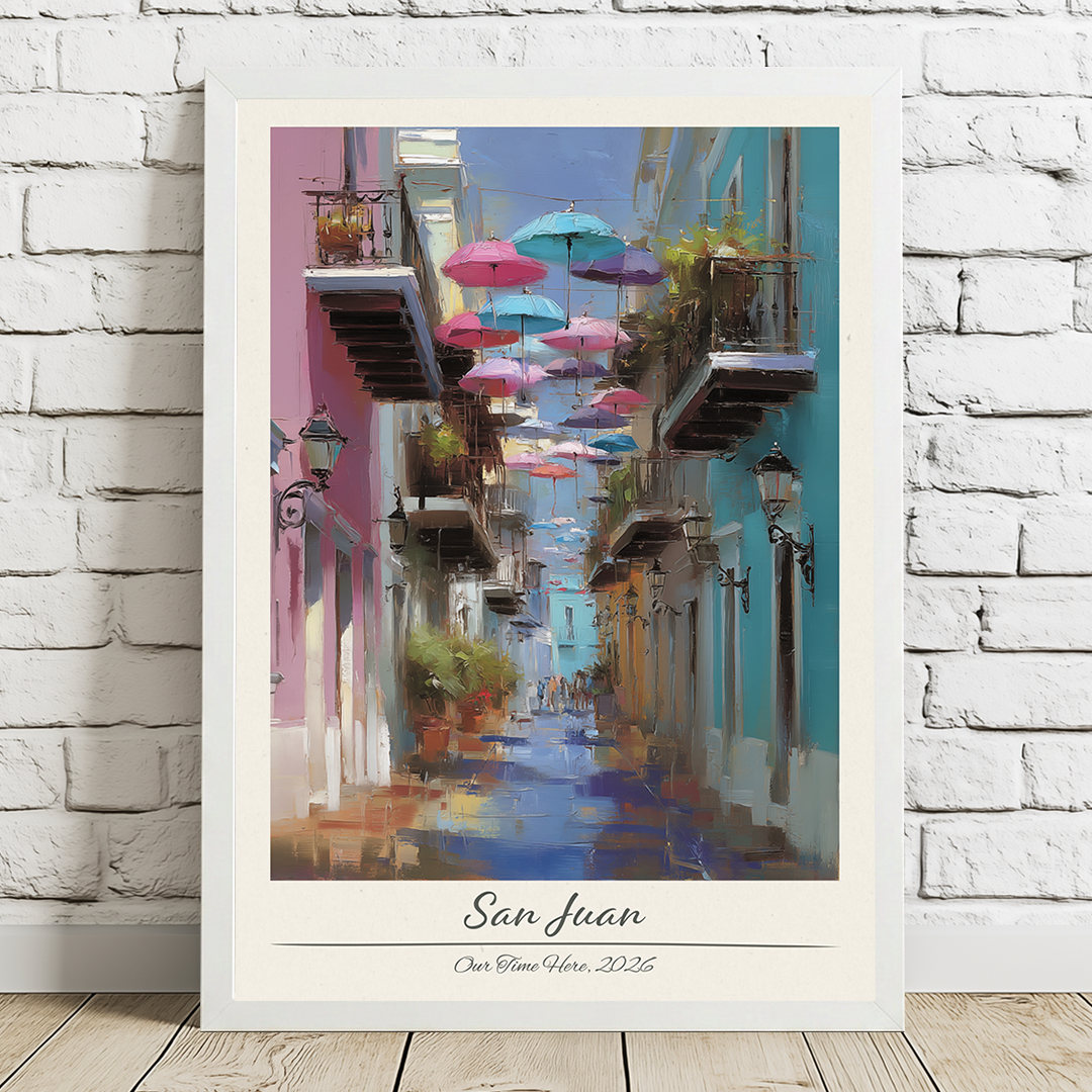 Framed artwork of a colorful street scene with umbrellas in San Juan, displayed on a white brick wall.