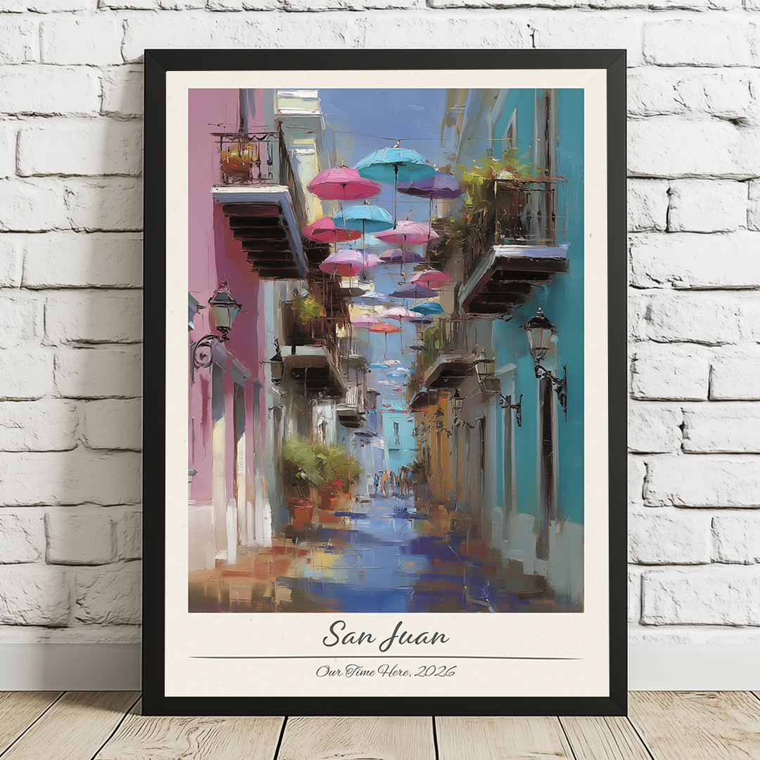 Framed artwork of a colorful street scene with umbrellas in San Juan, displayed on a white brick wall.