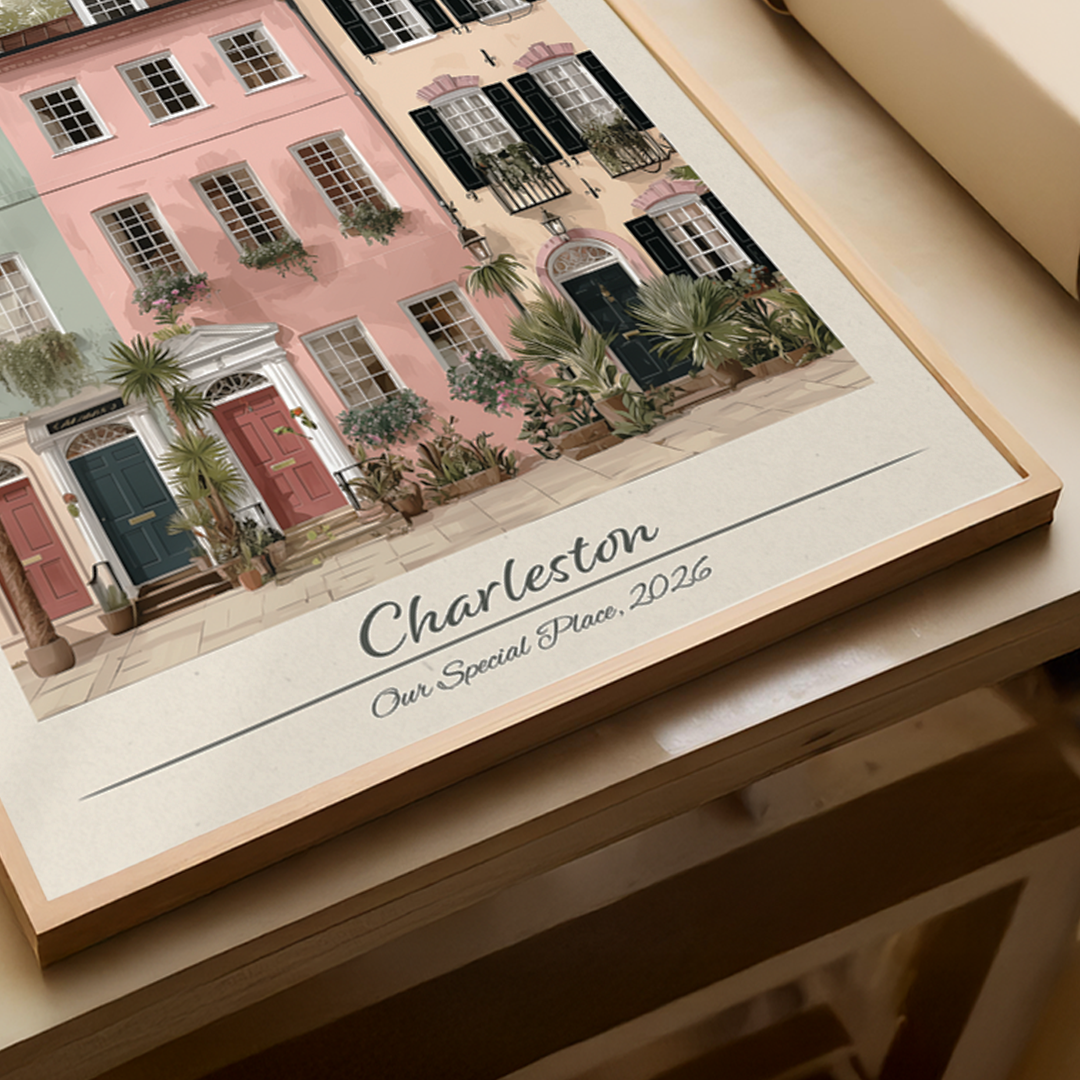 Framed artwork of a street scene with buildings and plants, featuring the text 'Charleston Our Special Place 2026'.