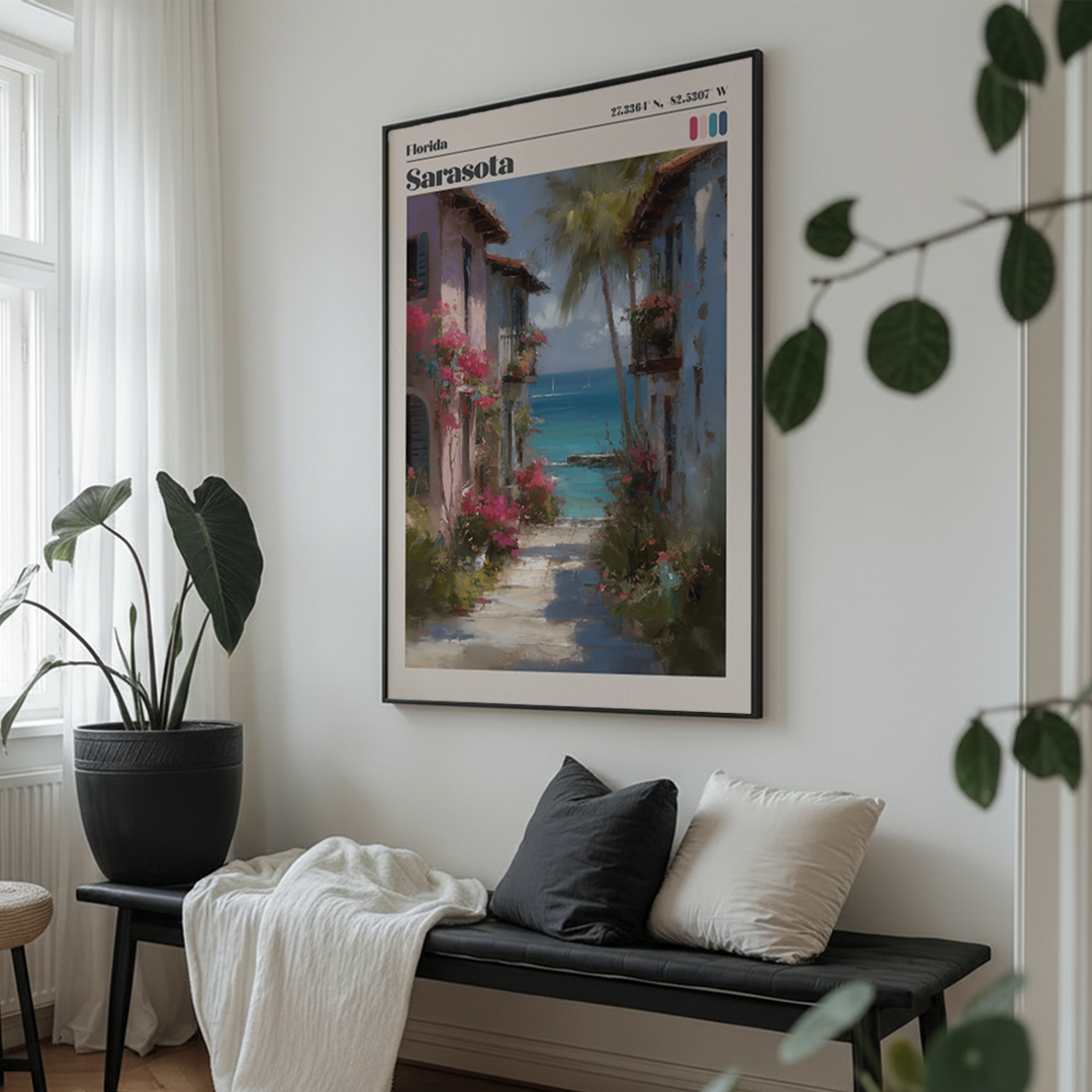 Framed artwork of a scenic street in Sarasota, Florida, above a bench with cushions in a room with plants.